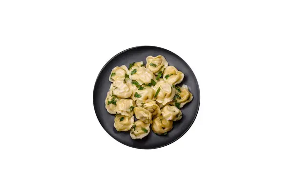 stock image Delicious fresh dumplings with turkey meat, with spices and herbs, parsley on a black plate against a dark concrete background