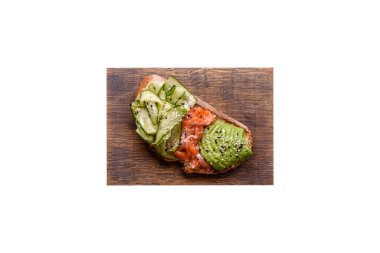 Delicious brown bread toast with salmon, avocado, cucumber and sesame seeds on a textured concrete background