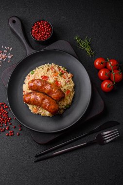 Izgarada pişirilmiş lezzetli tavuk ya da domuz sosisi. Koyu beton arka planda yulaf lapası ve sebzeler.