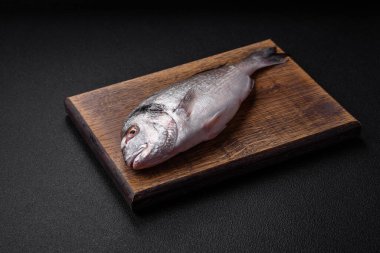 Taze çiğ dorada balığı, tuzlu, baharatlı ve otlu koyu beton arka planda.