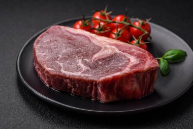 Taze çiğ biftek, tuz, baharat ve otlarla birlikte koyu beton bir arka planda.