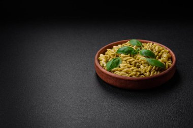 Koyu beton arka planda fesleğen, tuz ve baharatlı yeşil pesto soslu lezzetli taze makarna.