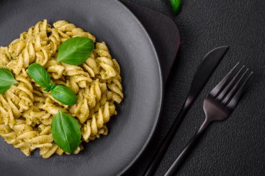 Koyu beton arka planda fesleğen, tuz ve baharatlı yeşil pesto soslu lezzetli taze makarna.