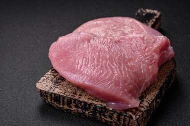 Tuz, baharat ve otlarla dilimlenmiş çiğ hindi eti, koyu beton arka planda.