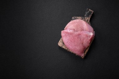 Tuz, baharat ve otlarla dilimlenmiş çiğ hindi eti, koyu beton arka planda.