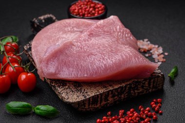 Tuz, baharat ve otlarla dilimlenmiş çiğ hindi eti, koyu beton arka planda.