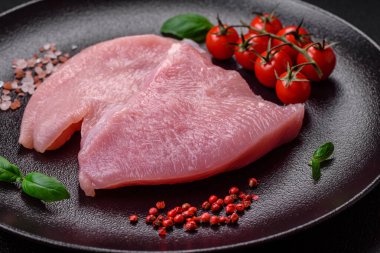 Tuz, baharat ve otlarla dilimlenmiş çiğ hindi eti, koyu beton arka planda.