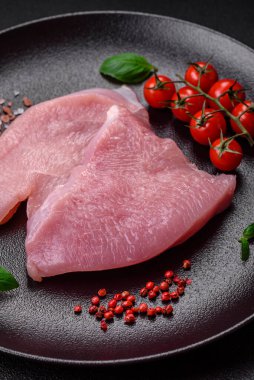 Tuz, baharat ve otlarla dilimlenmiş çiğ hindi eti, koyu beton arka planda.