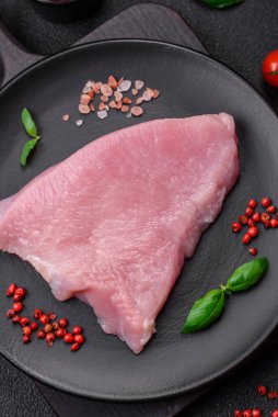 Tuz, baharat ve otlarla dilimlenmiş çiğ hindi eti, koyu beton arka planda.