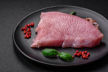 Tuz, baharat ve otlarla dilimlenmiş çiğ hindi eti, koyu beton arka planda.