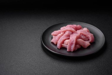 Tuz, baharat ve otlarla dilimlenmiş çiğ hindi eti, koyu beton arka planda.