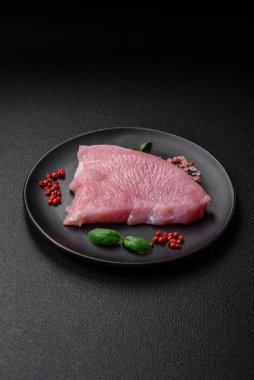 Tuz, baharat ve otlarla dilimlenmiş çiğ hindi eti, koyu beton arka planda.