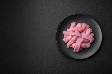 Tuz, baharat ve otlarla dilimlenmiş çiğ hindi eti, koyu beton arka planda.