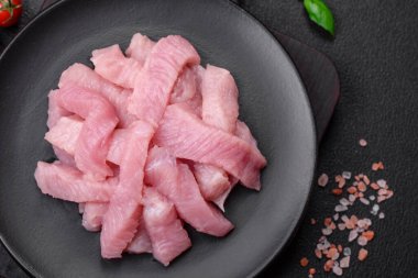 Tuz, baharat ve otlarla dilimlenmiş çiğ hindi eti, koyu beton arka planda.