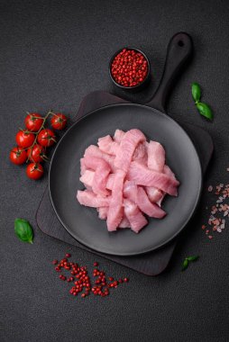 Tuz, baharat ve otlarla dilimlenmiş çiğ hindi eti, koyu beton arka planda.