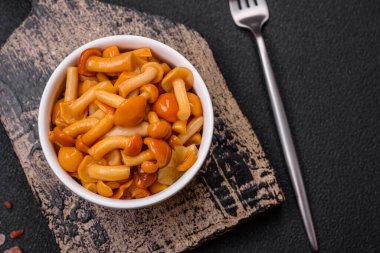 Koyu dokulu bir arka planda seramik tabakta tuz ve baharatla lezzetli ballı mantar turşusu.