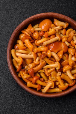 Koyu dokulu bir arka planda seramik tabakta tuz ve baharatla lezzetli ballı mantar turşusu.