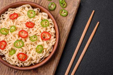 Lezzetli Asya mutfağı. İçinde pirinç, erişte, biber, mantar ve baharatlar var. Koyu beton arka planda.