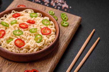 Lezzetli Asya mutfağı. İçinde pirinç, erişte, biber, mantar ve baharatlar var. Koyu beton arka planda.