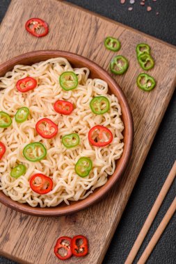 Lezzetli Asya mutfağı. İçinde pirinç, erişte, biber, mantar ve baharatlar var. Koyu beton arka planda.