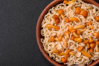 Lezzetli Asya mutfağı. İçinde pirinç, erişte, biber, mantar ve baharatlar var. Koyu beton arka planda.