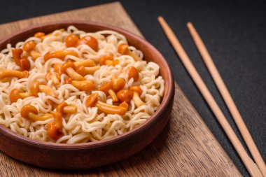 Lezzetli Asya mutfağı. İçinde pirinç, erişte, biber, mantar ve baharatlar var. Koyu beton arka planda.