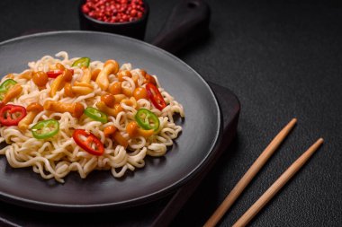 Lezzetli Asya mutfağı. İçinde pirinç, erişte, biber, mantar ve baharatlar var. Koyu beton arka planda.