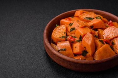 Lezzetli haşlanmış tatlı patates, tuz, baharat ve bitki küpleri seramik tabakta koyu beton arka planda.