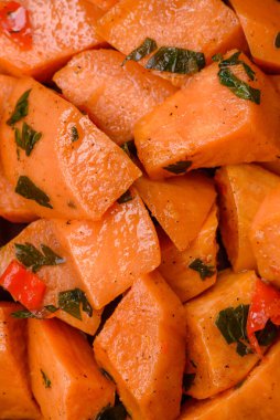 Lezzetli haşlanmış tatlı patates, tuz, baharat ve bitki küpleri seramik tabakta koyu beton arka planda.