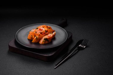 Lezzetli haşlanmış tatlı patates, tuz, baharat ve bitki küpleri seramik tabakta koyu beton arka planda.