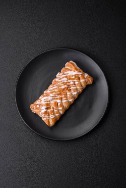 Lezzetli çıtır çıtır örülmüş çörek, içinde kuru üzüm, dışında beyaz krema, koyu beton arka planda.