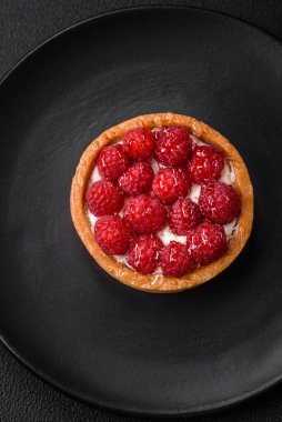 Olgun ahududu ve kremalı lezzetli, taze, yuvarlak turta. Koyu beton arka planda.