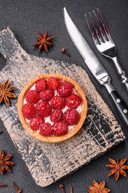 Olgun ahududu ve kremalı lezzetli, taze, yuvarlak turta. Koyu beton arka planda.