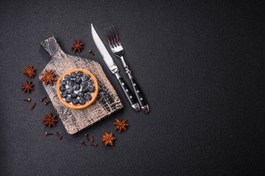 Olgun yaban mersinli ve kremalı lezzetli yuvarlak turta, koyu beton bir arka planda.