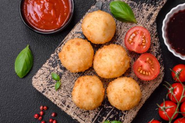 Lezzetli yuvarlak mozzarella topları ve parmesan peyniri, tuzlu ve ekşi baharatlı koyu beton arka planda. Fast food, sağlıksız yemek