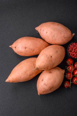 Koyu arkaplanda domates ve baharatlı taze, büyük, pembe patates şişeleri. Sağlıklı bir vejetaryen yemeği pişirmek.