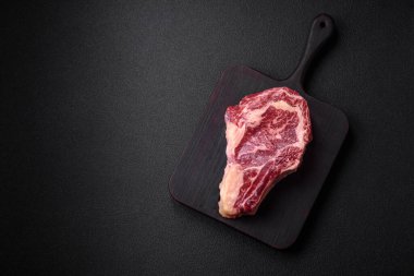 Taze, sulu, çiğ biftek, tuzlu ve baharatlı, koyu beton bir arka planda.