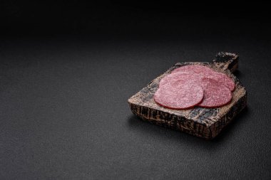 Tuzlu ve baharatlı lezzetli füme sosis koyu beton arka planda dilimler halinde kesilmiş.