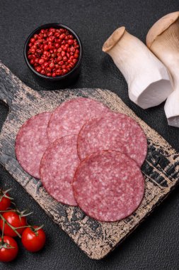 Tuzlu ve baharatlı lezzetli füme sosis koyu beton arka planda dilimler halinde kesilmiş.