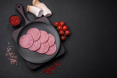 Tuzlu ve baharatlı lezzetli füme sosis koyu beton arka planda dilimler halinde kesilmiş.