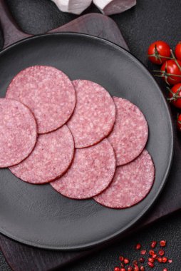 Tuzlu ve baharatlı lezzetli füme sosis koyu beton arka planda dilimler halinde kesilmiş.