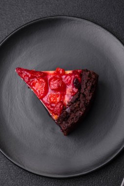 Koyu beton arka planda seramik tabakta kirazlı güzel bir dilim cheesecake.