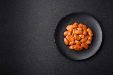 Beyaz bir seramik kasede, koyu beton bir arka planda domatesin içindeki lezzetli konserve fasulyeler.