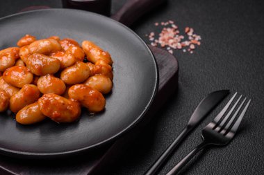 Beyaz bir seramik kasede, koyu beton bir arka planda domatesin içindeki lezzetli konserve fasulyeler.