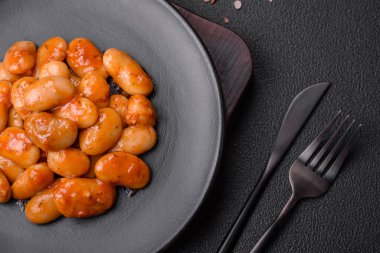 Beyaz bir seramik kasede, koyu beton bir arka planda domatesin içindeki lezzetli konserve fasulyeler.