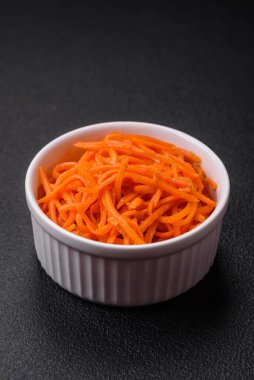 Lezzetli baharatlı havuçlar Kore usulü dilimlenmiş ve koyu beton arka planda seramik bir tabakta pişirilmiş.