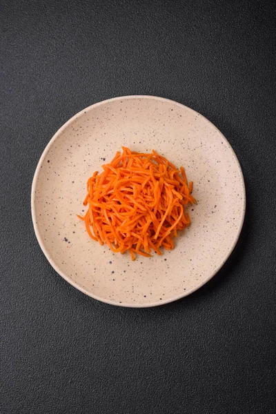 Delicious spicy carrots sliced and cooked in Korean style on a ceramic plate on a dark concrete background