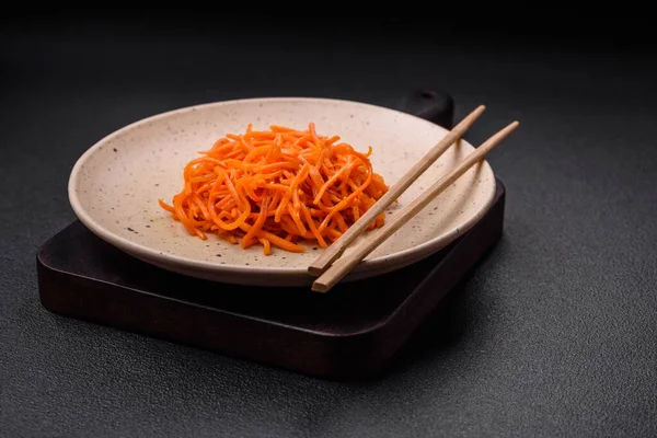 Delicious spicy carrots sliced and cooked in Korean style on a ceramic plate on a dark concrete background
