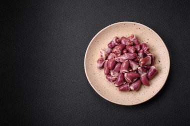 Taze çiğ tavuk, hindi ya da ördek kalbi seramik tabakta tuzlu ve baharatlı koyu beton arka planda.