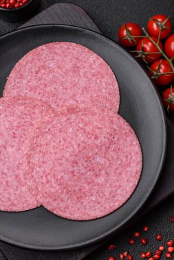 Lezzetli tütsülenmiş salam sosisi, tuz, baharat ve otlar koyu beton arka planda dilimler halinde kesilmiş.